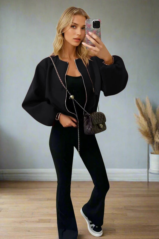 Woman in a black outfit taking a mirror selfie in a room with a gray wall and wooden floor.